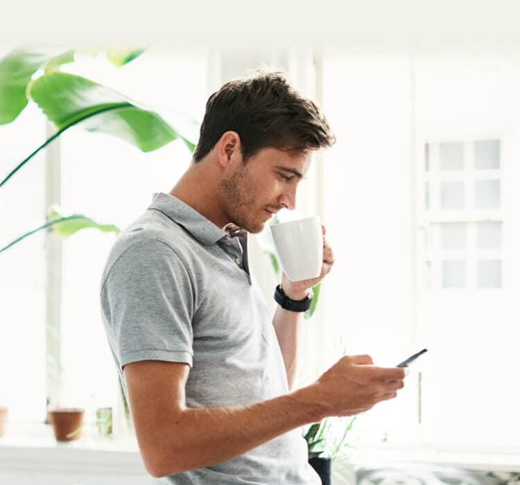 Muž pije kávu a drží mobilní telefon