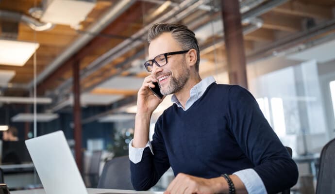 Usmívající se muž s mobilním telefonem u ucha dívající se na notebook