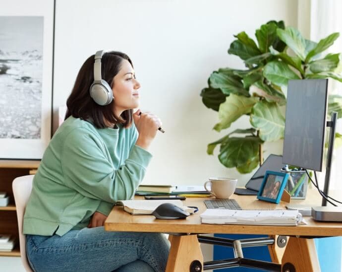 Žena se sluchátky na uších a perem v ruce, která se dívá na monitor počítače
