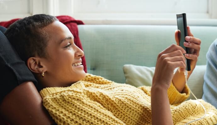 žena sedí na pohovce, dívá se na mobilní telefon a spouští produkt Norton 360 s aplikací AntiVirus Plus