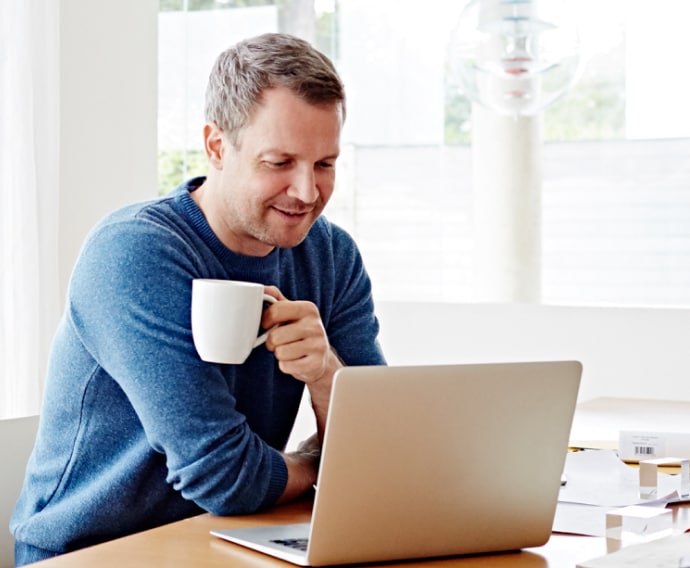 Muž doma používá notebook a pije kávu.